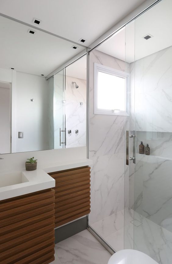 Banheiro com porcelanato que imita marmore carrara e movel de madeira