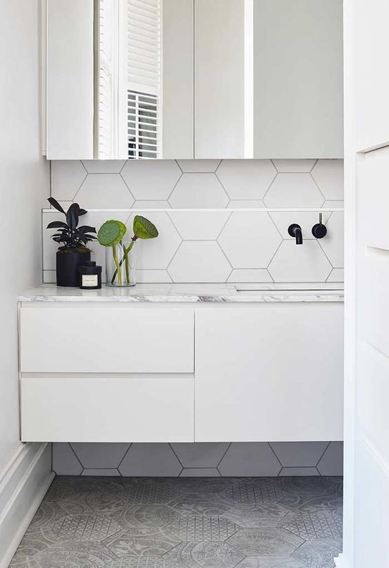 banheiro com revestimento hexagonal branco e cinza. E moveis brancos.
